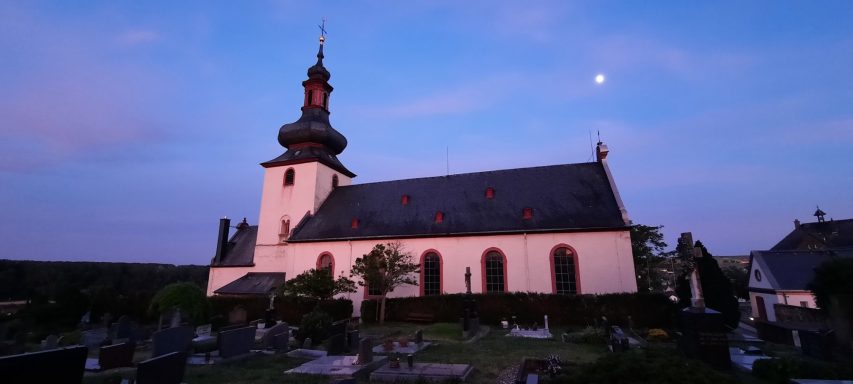 Feldsteinkirche mit Turm, umgeben von einem Friedhof, bei Dämmerungslicht.